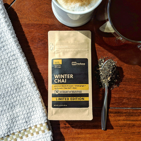 Retea Winter Chai premium spiced black tea blend with cardamom and ginger. Loose leaf bag provides 10 hours of education. Spoon of spices on wood table.